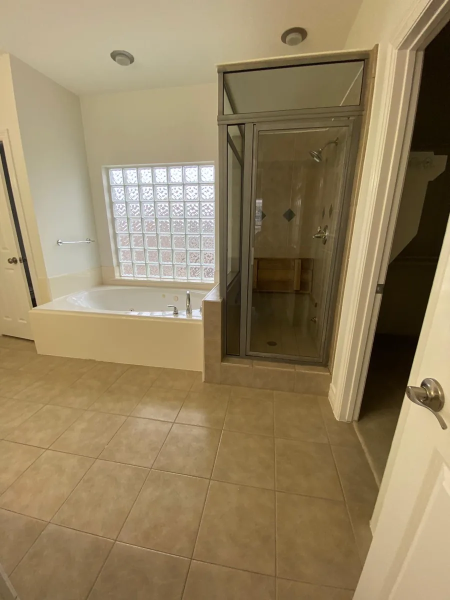 An empty, spotless bathroom with a clean tub, glass shower stall, and glass-block window