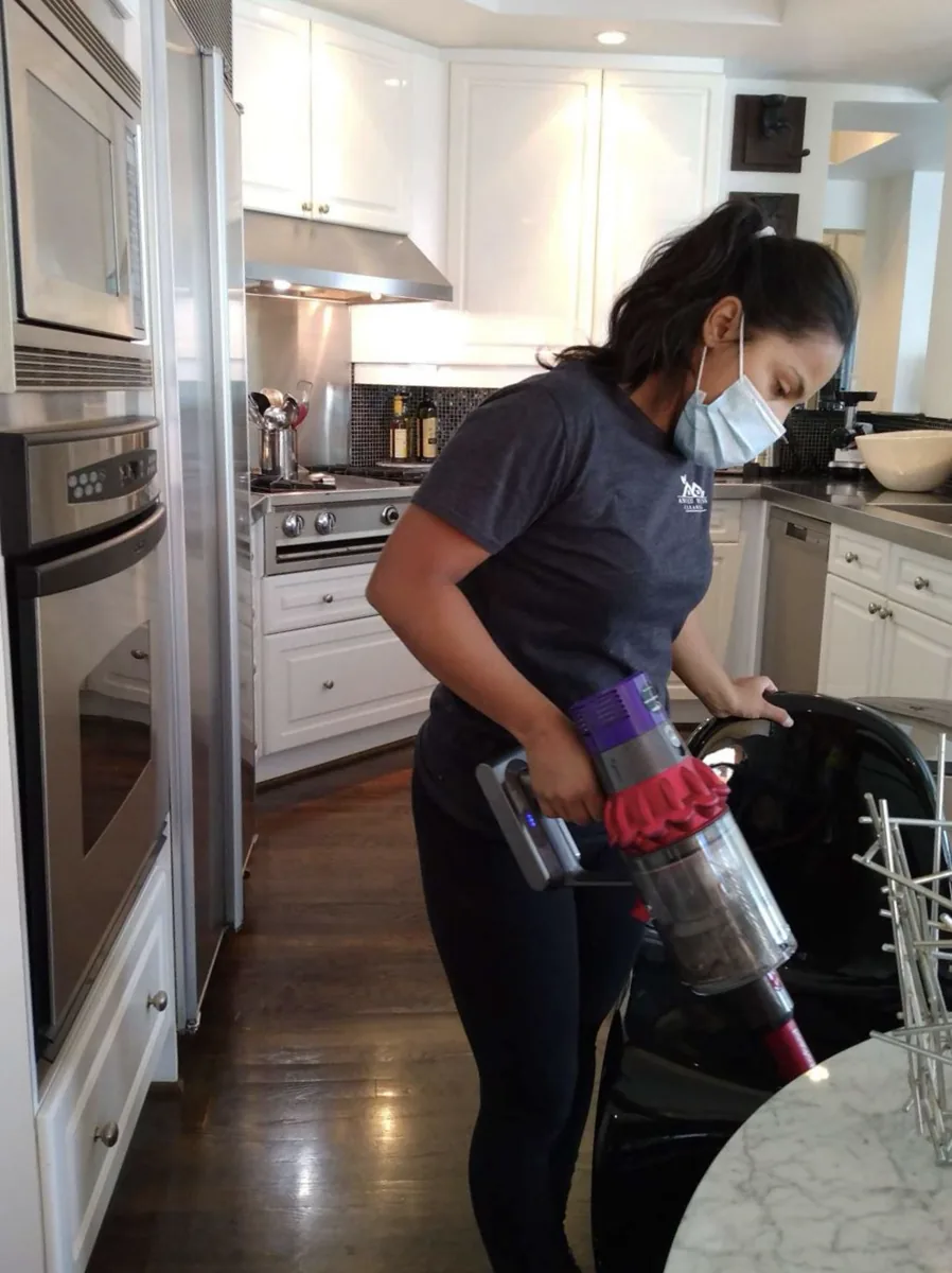 Anilu vacuuming the floor of a bright white kitchen with a cordless stick vacuum