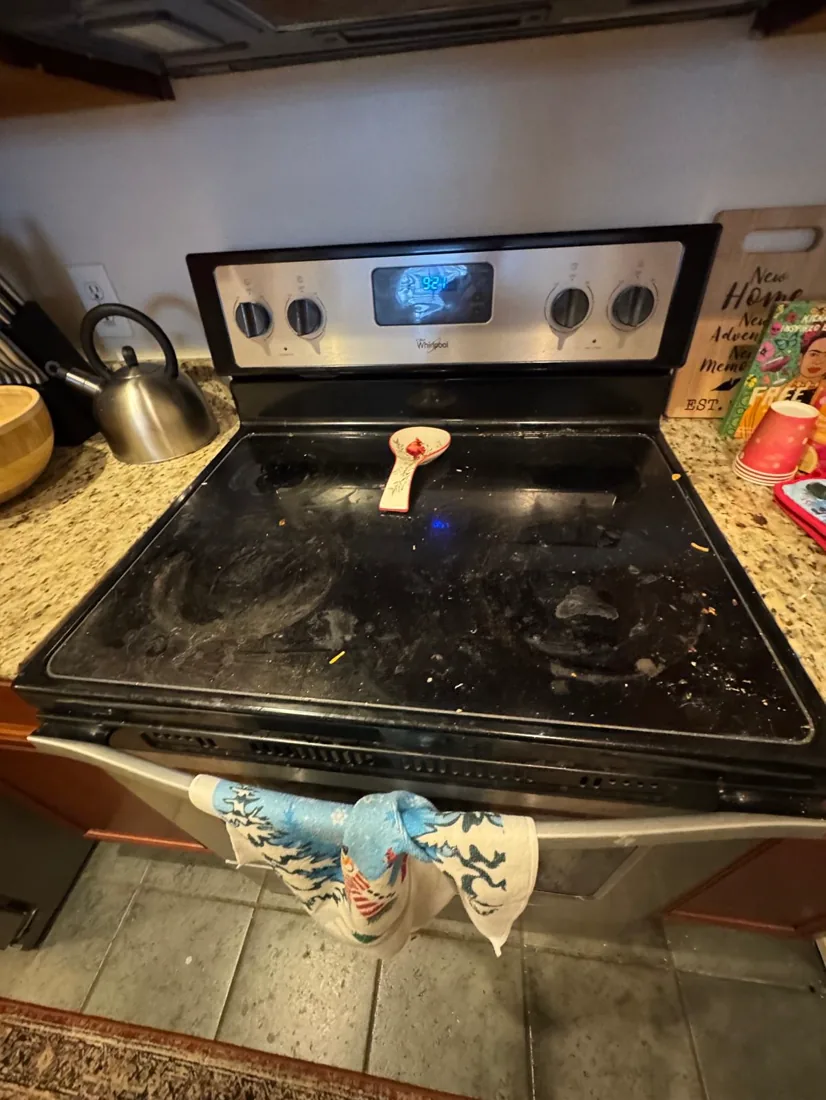 A greasy black stovetop scattered with crumbs before cleaning